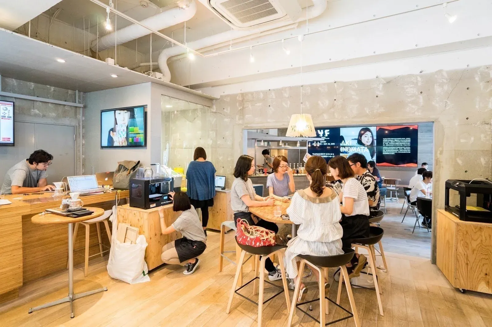Coworking space with wooden floor, shared tables and groups working on laptops