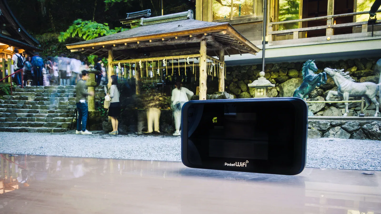 Black pocket wifi router on a table before a shrine gate and visitors