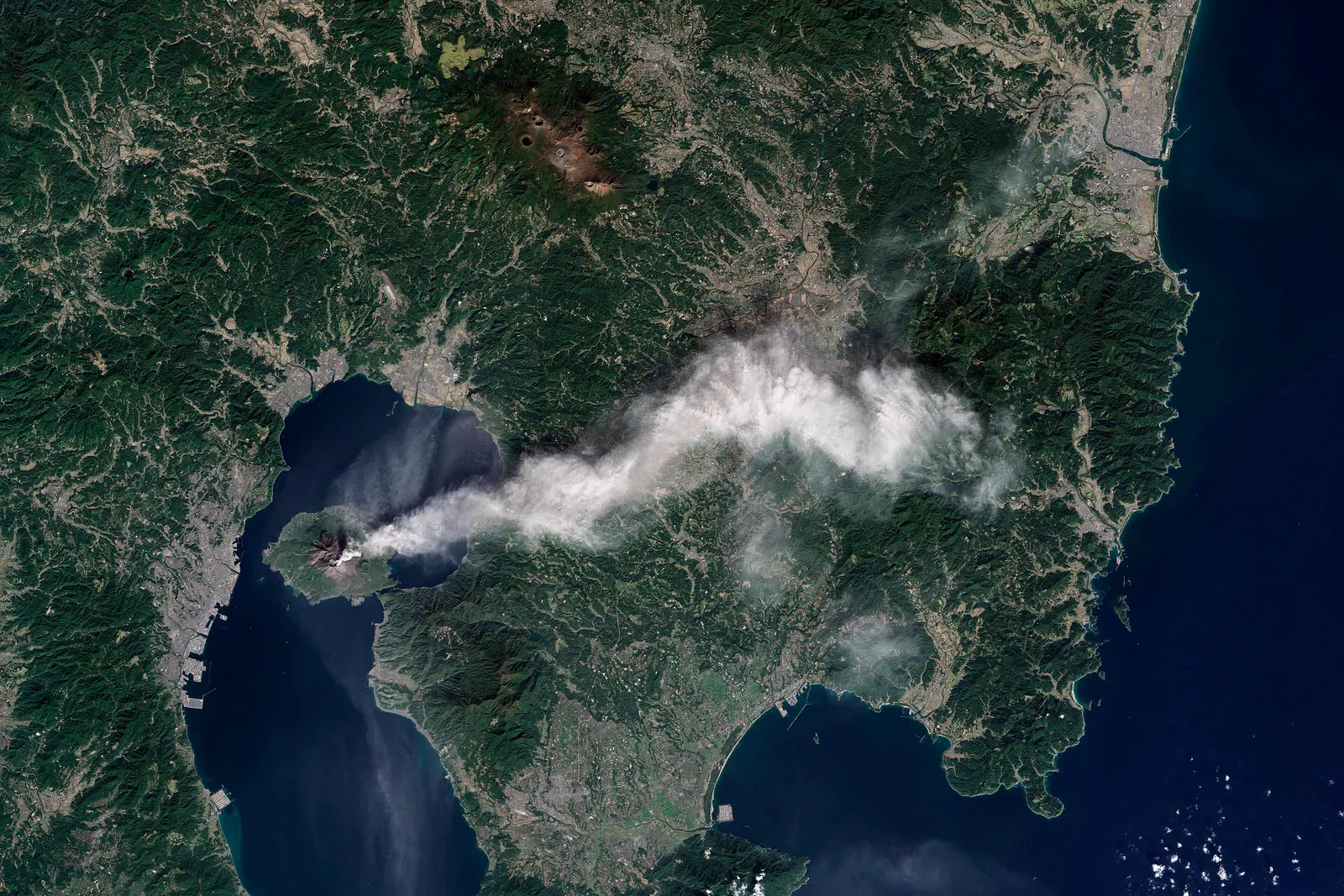 Satellite view of a volcanic ash plume over a peninsula and bay